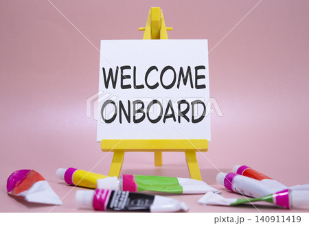 Welcome onboard symbol. Concept words Welcome onboard on wooden blocks. Beautiful pink background with paints and easel. Business and Welcome onboard concept. Copy space. 140911419