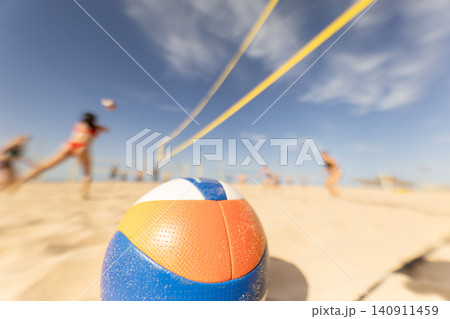 Group plays beach volleyball with a colorful ball under a blue sky on a sunny day Group plays beach volleyball with a colorful ball under a blue sky on a sunny day 140911459