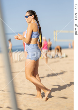 Woman on the beach enjoys volleyball activities in bright sunlight during a warm day surrounded by players Woman on the beach enjoys volleyball activities in bright sunlight during a warm day surrounded by players 140911464