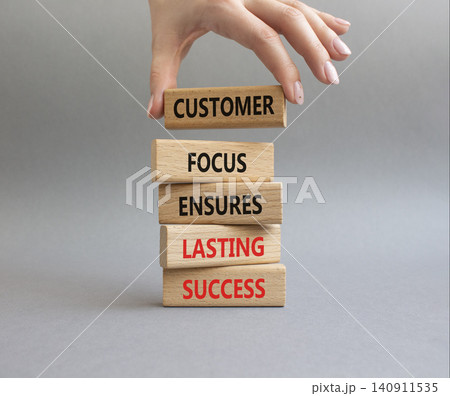 Customer Focus symbol. Wooden blocks with words Customer Focus Ensures Lasting Success. Businessman hand. Beautiful grey background. Businessman hand. Business and Customer Focus concept. Copy space 140911535