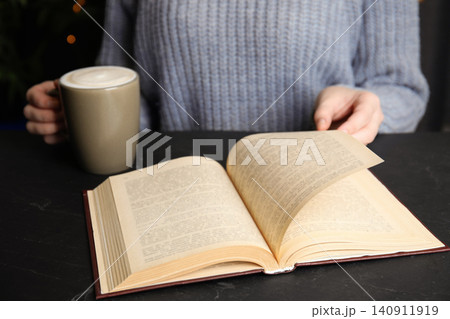Woman with cup of coffee reading book at table, closeup Woman with cup of coffee reading book at table, closeup 140911919