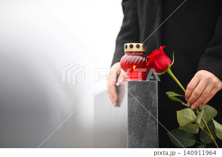 Woman holding red rose near black granite tombstone with candle outdoors, closeup. Funeral ceremony 140911964