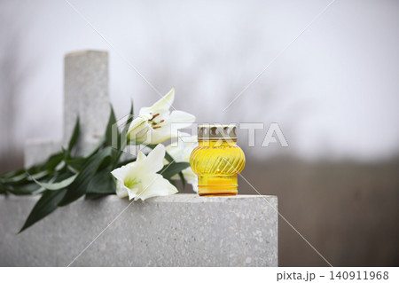 White lilies and candle on light grey granite tombstone outdoors. Funeral ceremony 140911968
