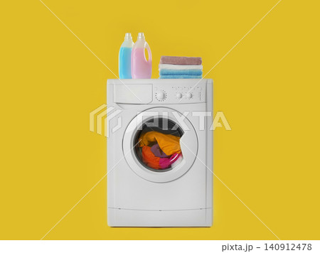 Modern washing machine with laundry, stack of towels and detergents on yellow background Modern washing machine with laundry, stack of towels and detergents on yellow background 140912478
