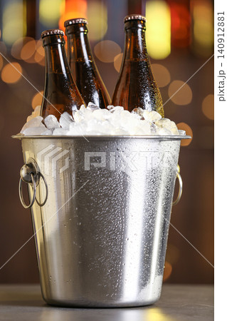 Beer in metal bucket with ice on table against blurred lights Beer in metal bucket with ice on table against blurred lights 140912881
