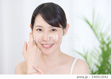 指で頬に触れながら肌の状態を確認する笑顔の女性 指で頬に触れながら肌の状態を確認する笑顔の女性 140913042