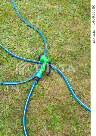 Garden hose with spray nozzle arranged on lawn for outdoor watering Garden hose with spray nozzle arranged on lawn for outdoor watering 140913300