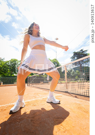 Woman practices tennis on a sunny day at a sports facility with clay courts and a clear blue sky 140913617