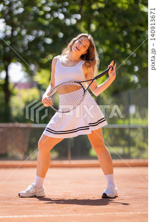 Young woman plays tennis on a sunny day at a local tennis court in a park setting with trees in the background 140913671