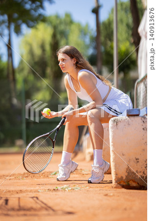 Tennis player sits on a bench holding a tennis ball during practice on a sunny day at a clay court Tennis player sits on a bench holding a tennis ball during practice on a sunny day at a clay court 140913676
