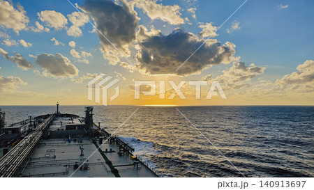 Horizontal wide shot of a large tanker vessel sailing into a dramatic sunset, with golden sunbeams breaking through cumulus clouds over a deep blue open sea Horizontal wide shot of a large tanker vessel sailing into a dramatic sunset, with golden sunbeams breaking through cumulus clouds over a deep blue open sea 140913697