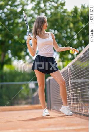 Young woman plays tennis on an outdoor court in a sunny location with green trees in the background Young woman plays tennis on an outdoor court in a sunny location with green trees in the background 140913716