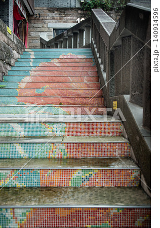 an outdoor stone staircase features vibrant, colorful mosaic tiled risers leading upward alongside a stone banister in an urban or historic setting. an outdoor stone staircase features vibrant, colorful mosaic tiled risers leading upward alongside a stone banister in an urban or historic setting. 140914596