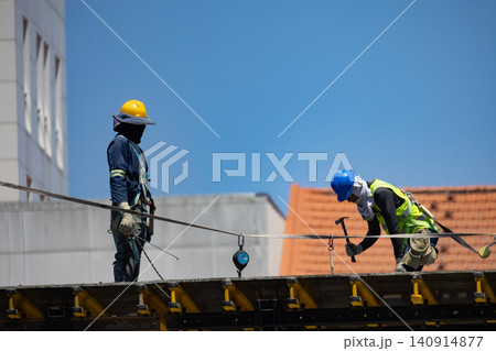 Workers perform construction tasks on a building site with safety gear during the day Workers perform construction tasks on a building site with safety gear during the day 140914877