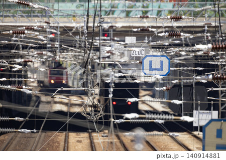 Trains move through a busy railway station with electric cables and many tracks in the background during a sunny day 140914881