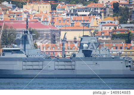 Naval ship docked near city buildings in sunny weather with clear skies during midday in a coastal area Naval ship docked near city buildings in sunny weather with clear skies during midday in a coastal area 140914885