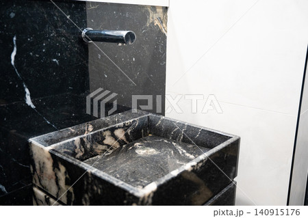 Modern marble sink with wall mounted faucet in a contemporary commercial restroom. Premium bathroom interior and sanitary design for office and public facilities Modern marble sink with wall mounted faucet in a contemporary commercial restroom. Premium bathroom interior and sanitary design for office and public facilities 140915176