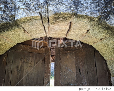A stone archway stands strong, framing a closed wooden gate. This structure highlights historic Spanish architecture and shows the effects of time and weather on the materials. 140915192