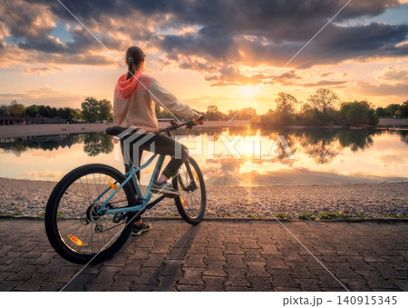 Woman riding a mountain bike near lake at sunset in summer Woman riding a mountain bike near lake at sunset in summer 140915345