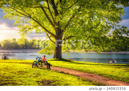 Woman sitting on bench and mountain bike, green trees Woman sitting on bench and mountain bike, green trees 140915358