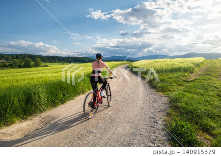 Woman riding mountain bike on dirt road and green wheat fields Woman riding mountain bike on dirt road and green wheat fields 140915379