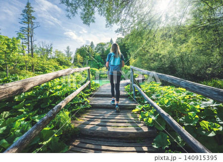 Woman with backpack walking along a wooden boardwalk in forest Woman with backpack walking along a wooden boardwalk in forest 140915395