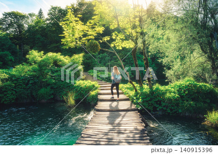 Woman with backpack on wooden boardwalk in green forest near lake Woman with backpack on wooden boardwalk in green forest near lake 140915396