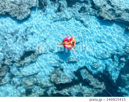 Aerial view of woman relaxing on pink inflatable ring in blue sea Aerial view of woman relaxing on pink inflatable ring in blue sea 140915415