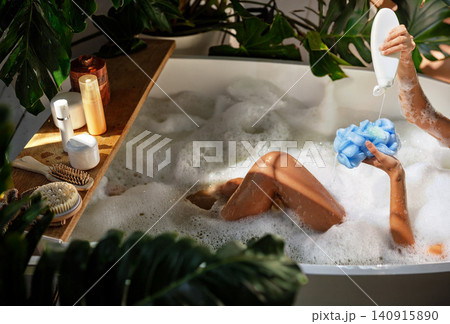 Caucasian young woman pouring body wash on sponge in bubble bath at home bathroom 140915890