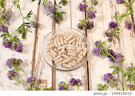 Alfalfa powder in capsules with a bouquet of flowers, a medicinal herbal composition, an alternative folk medicine concept, an advertisement for a green pharmacy, a collection of useful herbs 140918019