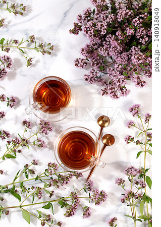 Medicinal herbal tea or Oregano infusion in a glass cup with flowers, alternative traditional medicine concept, estrogen source, menopause remedy, green pharmacy advertisement, 140918049