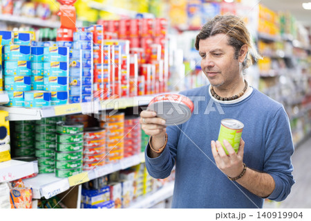 Adult man selects canned goods at grocery store Adult man selects canned goods at grocery store 140919904
