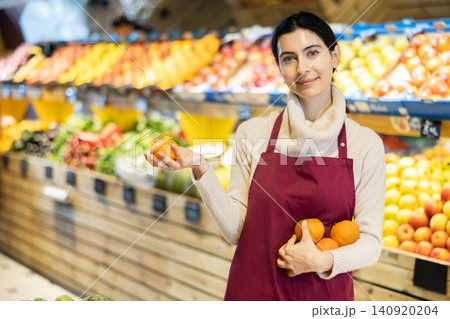 Young woman seller offers tangerines in vegetable shop Young woman seller offers tangerines in vegetable shop 140920204