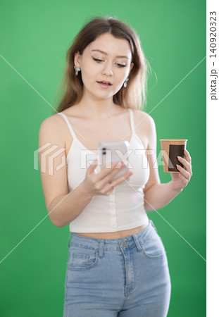Chroma key compositing. Pretty young woman drinking coffee and scrolling through her smartphone screen against green screen background. 140920323