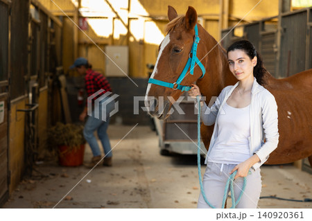 Woman with horse on leash in stable 140920361
