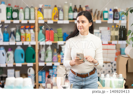 Woman holding phone and scrolling through product information on phone while standing in supermarket Woman holding phone and scrolling through product information on phone while standing in supermarket 140920413