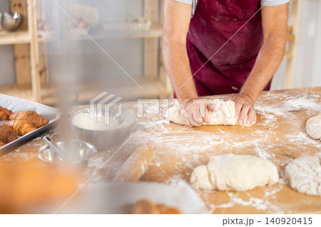 Unrecognizable senior man works in bakery as baker, kneads dough, works with flour. 140920415