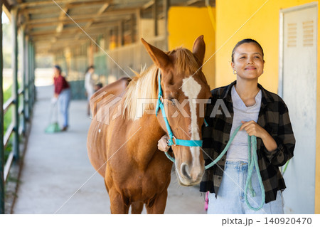 Young woman leading horse out of stable 140920470