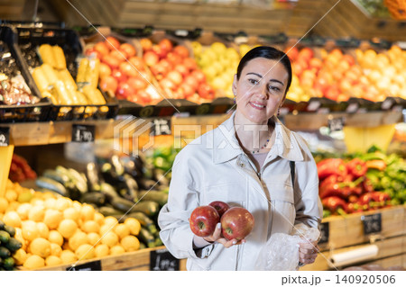Middle-aged woman holding red apples in grocery store Middle-aged woman holding red apples in grocery store 140920506