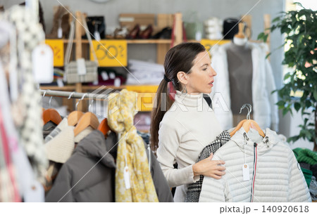 Selective middle-aged woman choosing something for autumn-winter in clothing store 140920618