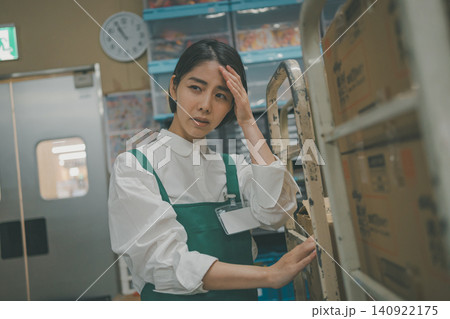 スーパーマーケットのバックヤードで頭痛に苦しむ若い女性スタッフ スーパーマーケットのバックヤードで頭痛に苦しむ若い女性スタッフ 140922175