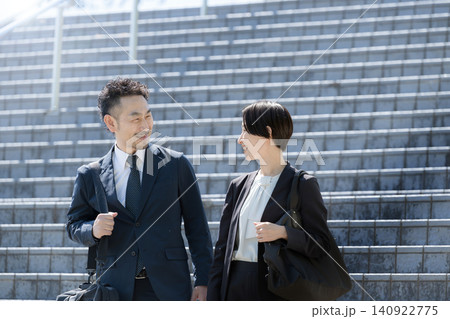 屋外で会話をしながらオフィス街へ歩く通勤する日本人ビジネスパーソン男女 会社員のライフスタイル 屋外で会話をしながらオフィス街へ歩く通勤する日本人ビジネスパーソン男女 会社員のライフスタイル 140922775