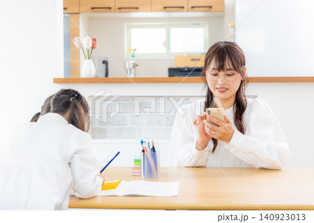 リビングで勉強する小学生の女の子とスマホを見るママ リビングで勉強する小学生の女の子とスマホを見るママ 140923013