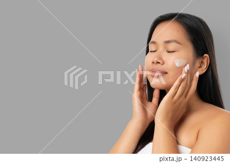 Woman applies skincare product on her face in a spa setting Woman applies skincare product on her face in a spa setting 140923445