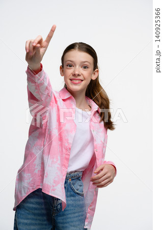 Smiling teenage girl pointing upward while looking at camera. Smiling teenage girl pointing upward while looking at camera. 140925366