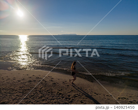 Young Woman Jogging on Sandy Beach at Sunrise along Sea Young Woman Jogging on Sandy Beach at Sunrise along Sea 140925450