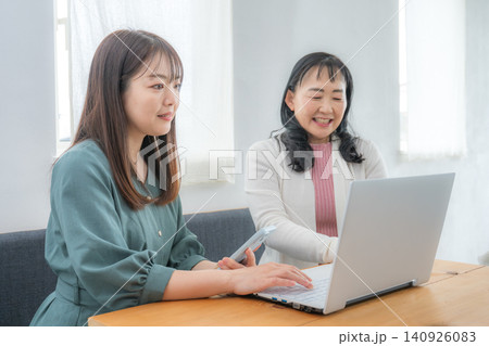 ノートパソコンを見ながら会話する二人の女性 140926083
