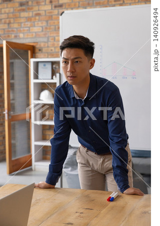 Asian man in his 30s leaning forward, pointing at whiteboard chart in office with navy shirt Asian man in his 30s leaning forward, pointing at whiteboard chart in office with navy shirt 140926494