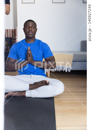African american man sitting and meditating on black yoga mat in living room African american man sitting and meditating on black yoga mat in living room 140927249