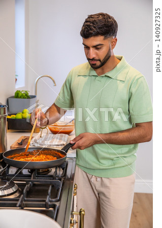 Indian man stirring tomato sauce in black nonstick pan with wooden spatula in bright kitchen Indian man stirring tomato sauce in black nonstick pan with wooden spatula in bright kitchen 140927325